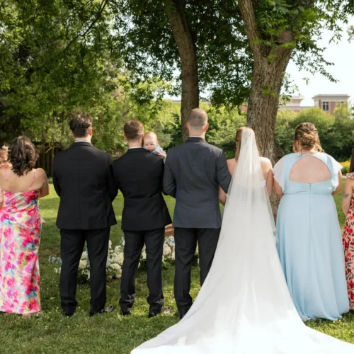 a wedding photo of Carrie's kids. They stand with their spouses with their backs facing the camera. Several hold Carrie's grandchildren in their arms.