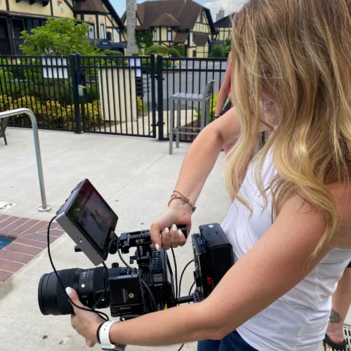 Abbey laughing with a video camera shooting a scene. The camera is comically large compared to Abbey's small stature.
