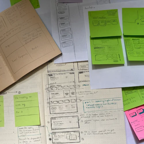 Multiple sketchbooks and pieces of paper spread out on a table to show the wireframes and interface notes for multiple different websites.