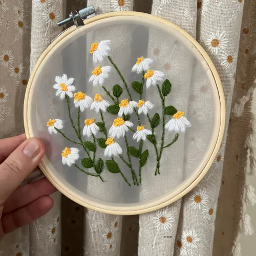 fabric in an embroidery hoop featuring embroidered white and yellow daisies