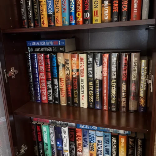 A tidy book shelf displaying an extensive collection of James Patterson books
