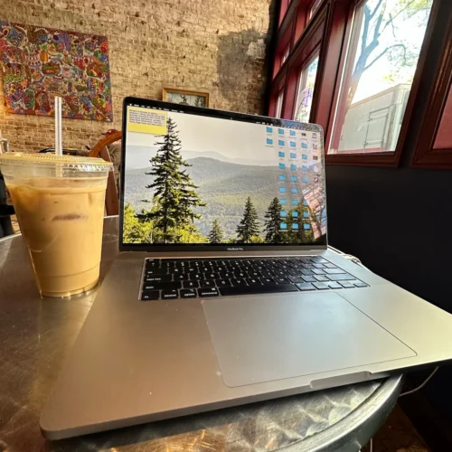 An iced coffee and a macbook pro on a small table in a local cafe