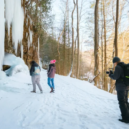 Sarah Grimm photographing hikers in front of large icicles on a hiking path during the winter co-op shoot