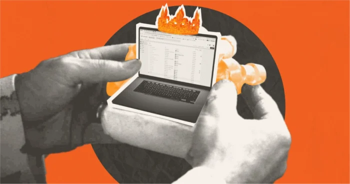 Hands holding a small laptop with a crown on it, against an orange background.
