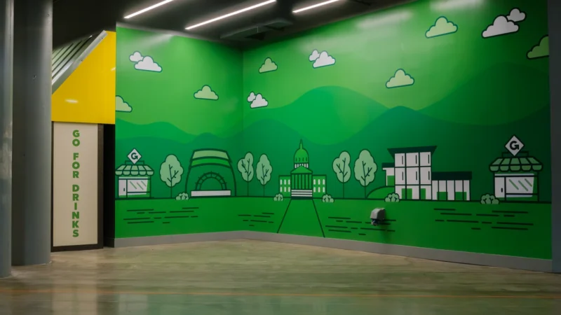 A branded engagement space within the Charleston Civic Center. Floor-to-ceiling vinyl clings compose a colorful illustrated mural. The mural depicts a stylized town. The Appalachian mountains are visible in the background, and light  stylized clouds float above the scene.

Beside the mural, directional signage is visible for the GoMart Grab N' Go drink coolers.