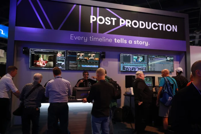 People working at a post-production booth with multiple screens displaying video editing software at NAB 2025 event.