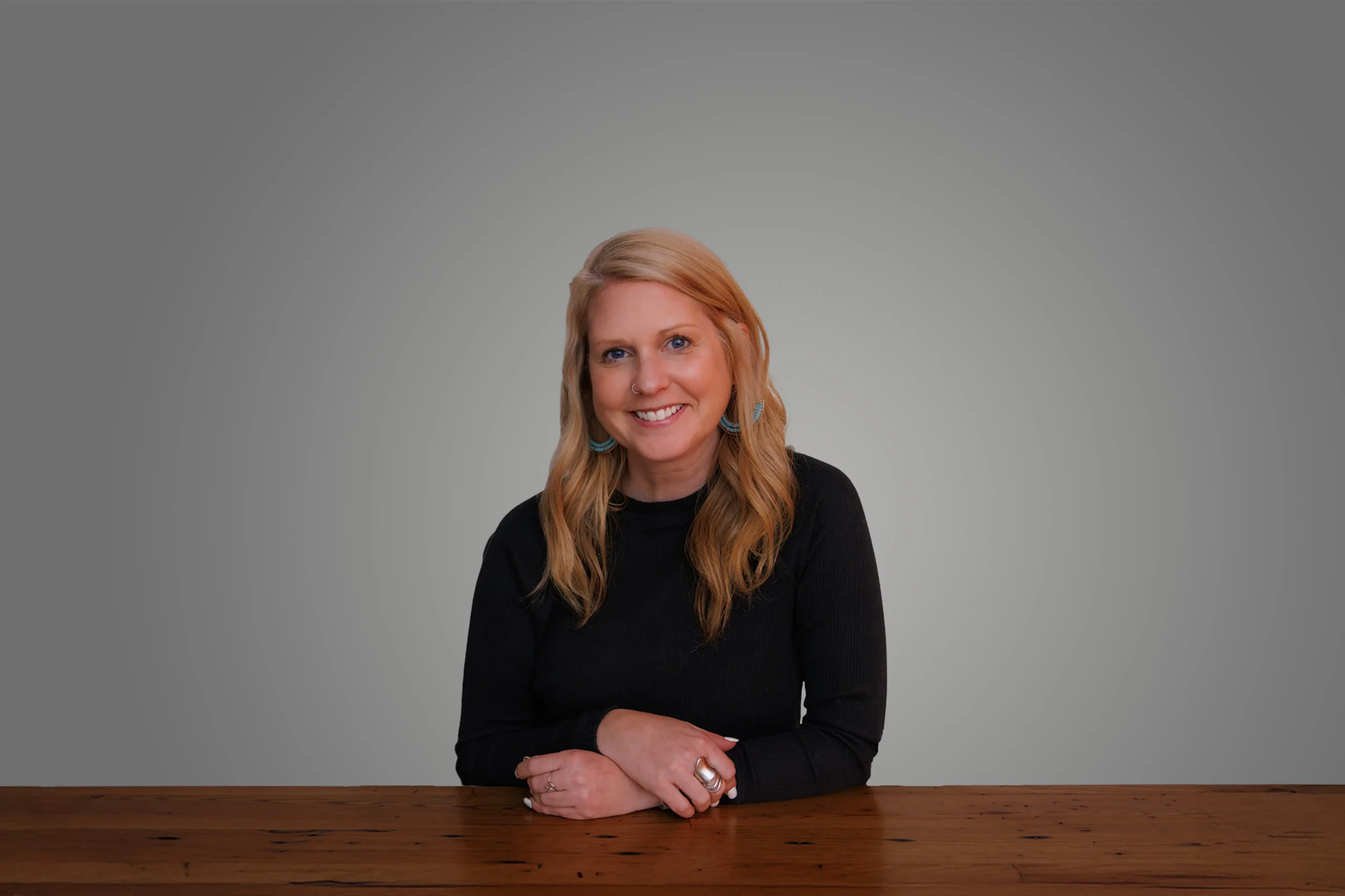 Abbey Reifsnyder smiling, seated at a wooden table, with a neutral gray background.