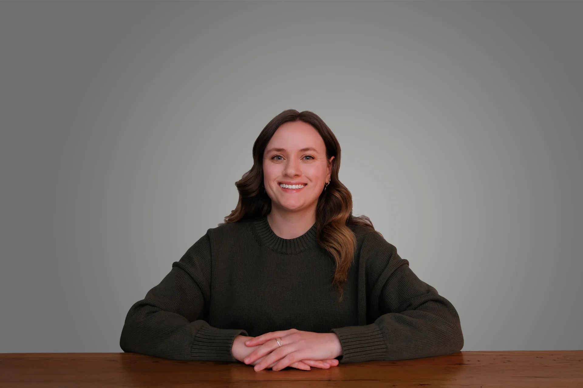 Alexa Nagy, seated at a table, smiling against a gray background, wearing a dark sweater.