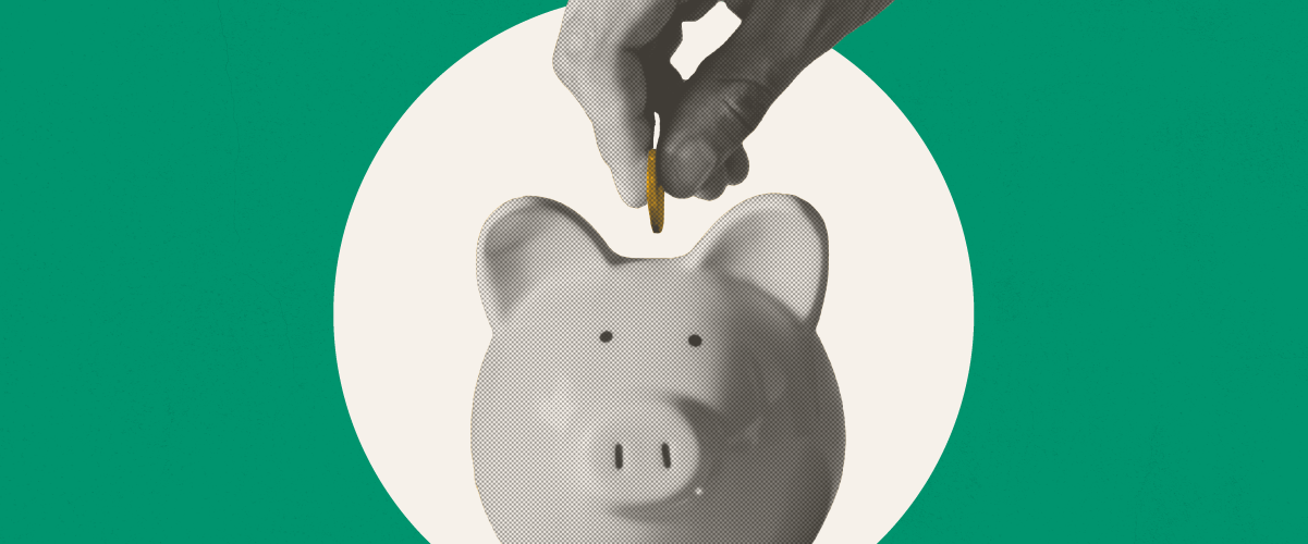 Hand inserting a coin into a white piggy bank against a green background.