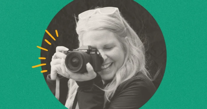 Woman with blonde hair smiling while holding a camera up to photograph, circular portrait on green background.