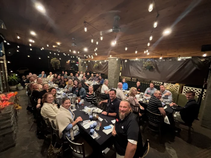 Large group of people dining together at an outdoor patio restaurant at night, with string lights overhead.