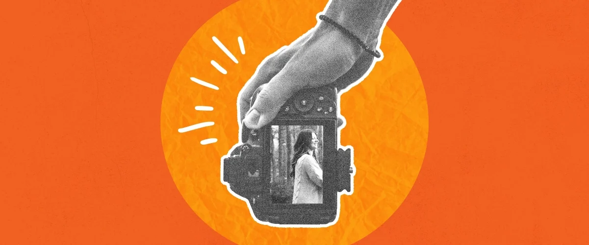 Hand holding a vintage camera with a small figure visible inside the lens, on an orange background.