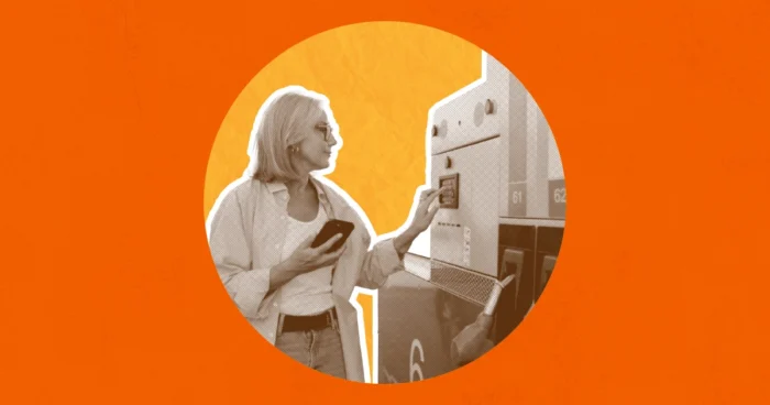 Woman using a kiosk or ATM machine while holding a smartphone, depicted in monochrome against an orange background.