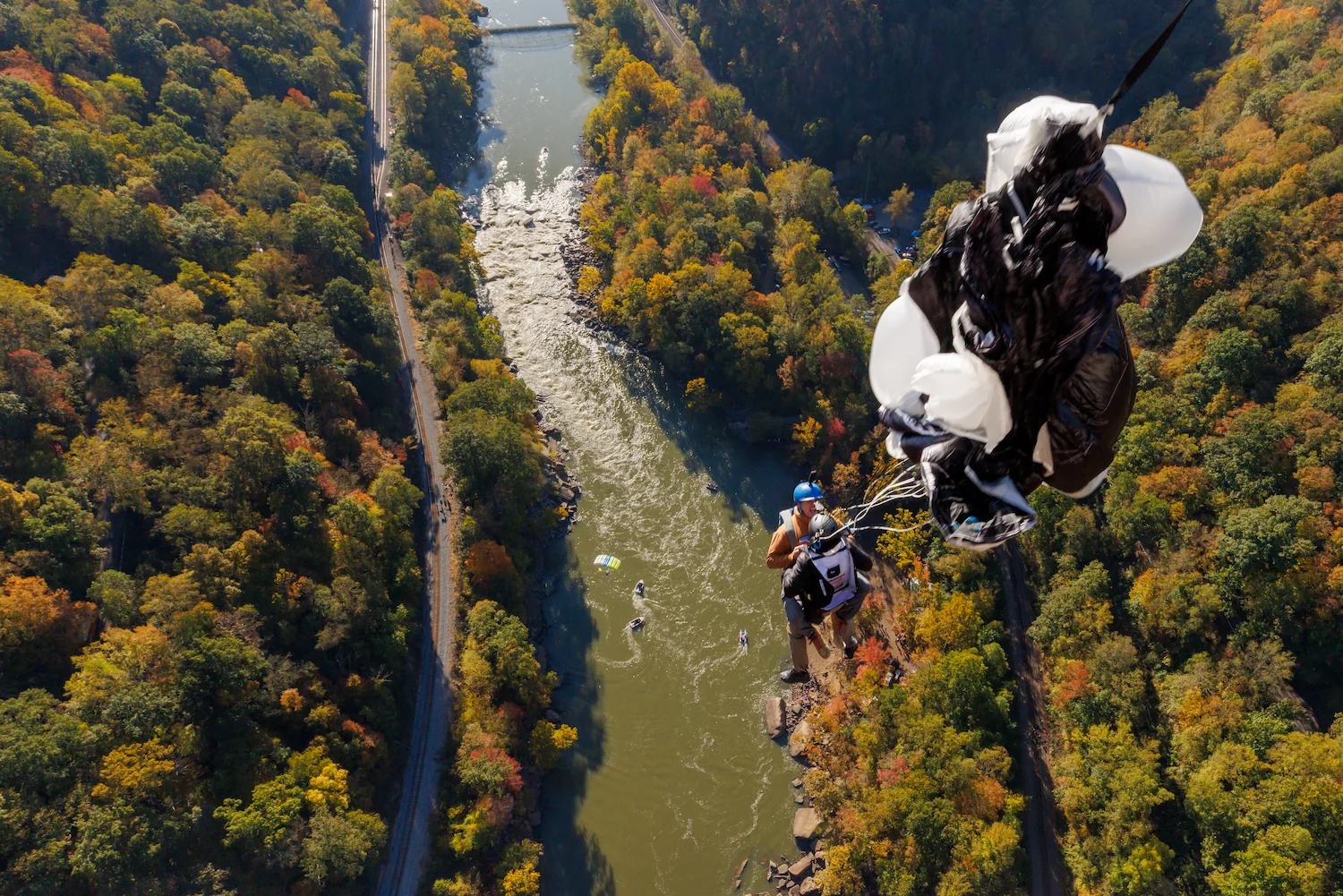 Aerial view of a BASE jumper leaping from a cliff above a river gorge surrounded by autumn foliage, parachute deploying.